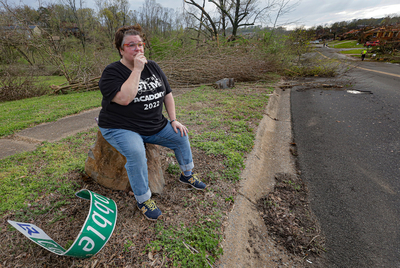 Kamrin O’Neill fights to hold back tears while resting from walking around her neighborhood after a tornado tore through west Little Rock on Friday, March 31, 2023. O'Neill's home on Cobble Hill Road was heavily damaged. The twisted Cobble Hill street sign lays at her feet. (John Sykes/Arkansas Advocate)