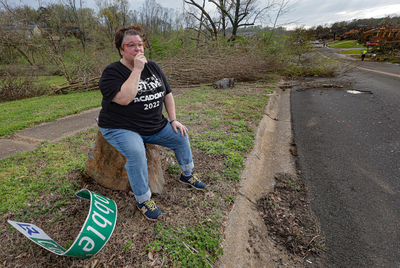 Kamrin O’Neill fights to hold back tears while resting from walking around her neighborhood after a tornado tore through west Little Rock on Friday, March 31, 2023. O'Neill's home on Cobble Hill Road was heavily damaged. The twisted Cobble Hill street sign lays at her feet. (John Sykes/Arkansas Advocate)